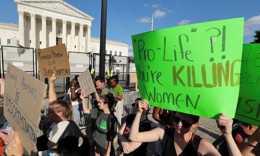 A crowd marches with signs in front of the Supreme Court. The next reads, on lime green poster board, 'Pro-Life?! You kill women'.