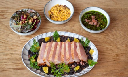Thick slices of pork over black beans on a large pie plate, with three small bowls of chimichurri, farrova, and salad.
