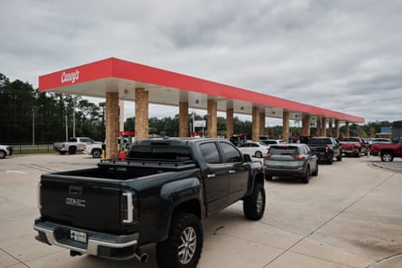 cars line up at gas station with cloudy sky above