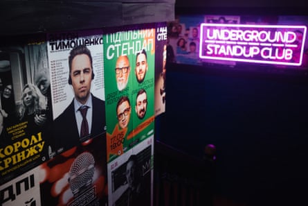 Posters advertising comedian’s shows next to an illuminated pink sign saying ‘underground standup club’