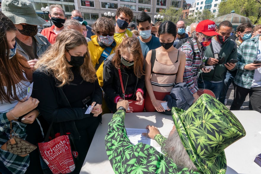 A man wearing a cannabis costume hands out marijuana cigarettes to a crowd around a table in New York