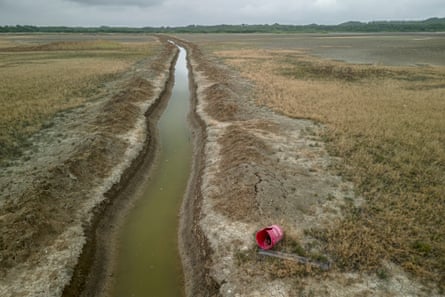 A channel of water runs between two banks of land that are made up of mud and sparse barren grass