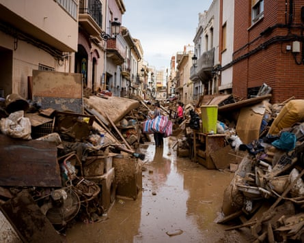 A narrow residential street covered in mud with ruined belonging piled up on both sides