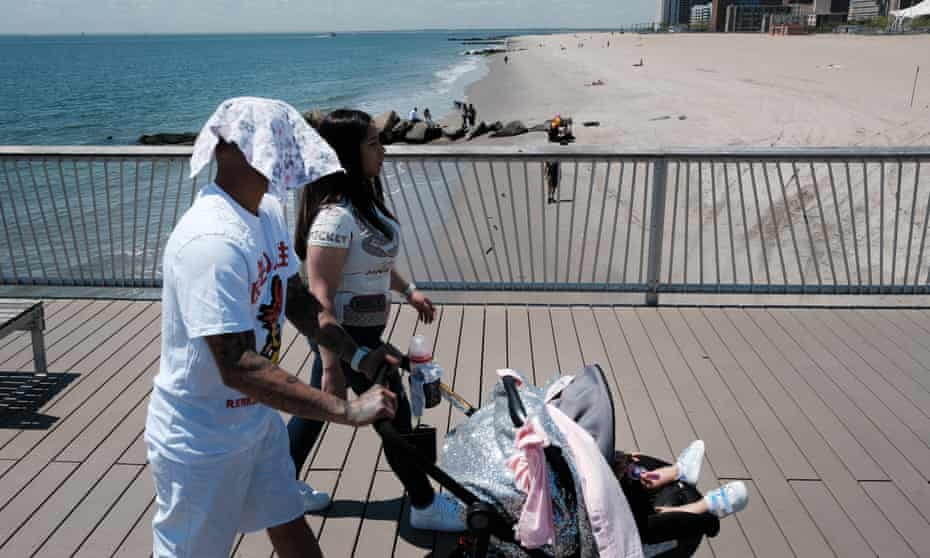 family walks on boardwalk with beach in the background. Man has cloth on his head