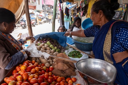 A woman serving a customer reaches over to a pile of vegetables.