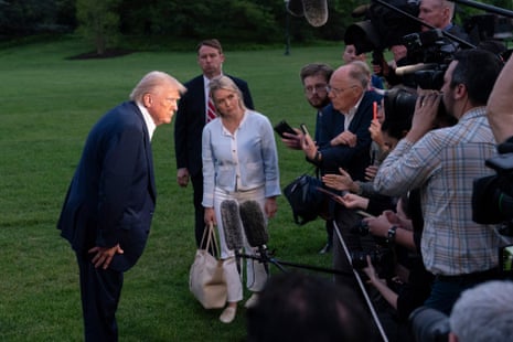 a man in a suit leans towards a group of people holding phones, cameras and microphones