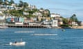 Rowers on the water with a backdrop of colourful houses on a hill, at the Dartmouth regatta in Devon