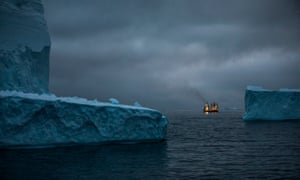 Two ships side by side, lit up at night, between two icebergs