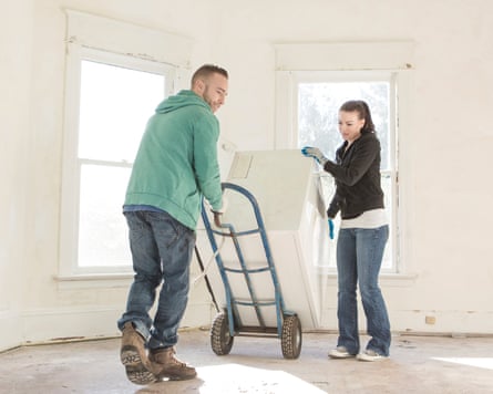 A couple use a sack truck to move a large white heavy item in a house.