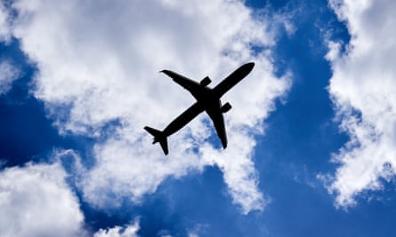 A silhouette of a plane against a blue sky with clouds