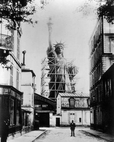 black and white photograph of a street with the statue behind the rooftops