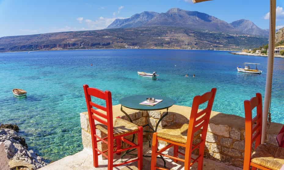 A table for two on a terrace overlooking the sea and, in the distance, mountains in Greece. To promote a food tour of Greece by Intrepid Travel.