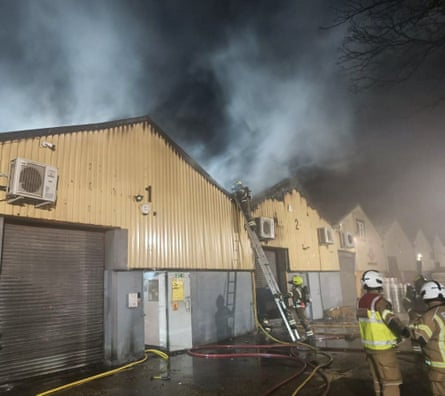 Firefighters at the warehouse, with dark smoke billowing above it