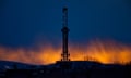 A drilling rig is silhouetted at sunset.