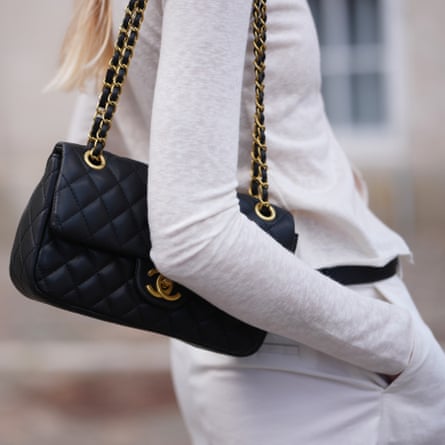 A woman wears a black quilted leather Chanel bag with a chain strap.