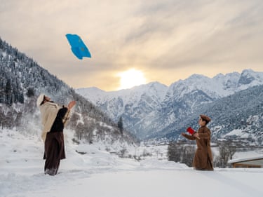 Two men fly a kite in a snowy mountain valley