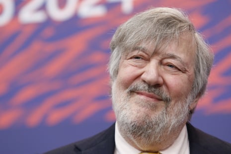 Stephen Fry, with a long fringe and close-cropped beard, squints slightly as he smiles