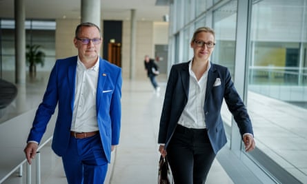 Tino Chrupulla and Alice Weidel walk down a hallway looking at the camera