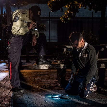 A policeman searches a homeless man suspected of stabbing a person in order to rob him