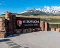 A large sign reading 'Yellowstone National Park' with the National Park Service logo at the north entrance, with snow-capped mountains behind.