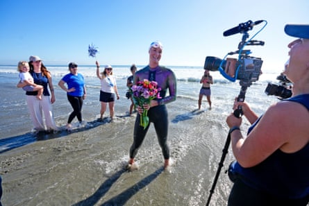 A woman smiles while holding flowers on a beach.