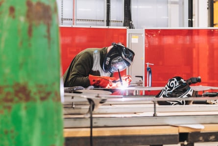 A welder looks closely at their work, with a bright arc of flame