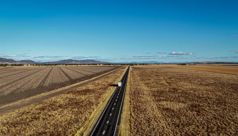 A drone shot of the truck on a long straight road between fields