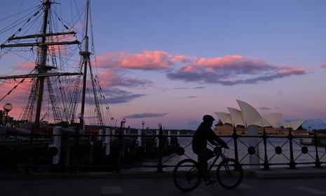 A lone person rides a bicycle past the Sydney Opera House in Sydney at sunset