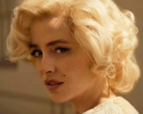 Dakota Johnson with platinum blonde curled hair and light makeup looks to the side in soft lighting