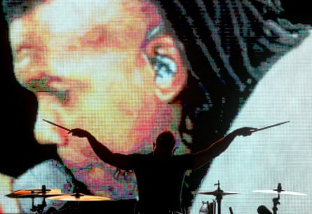 A silhouette of a drummer in front of a projection of a singer