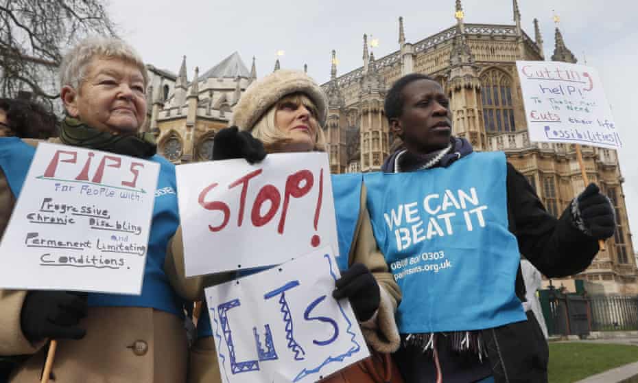 Protesters against disability benefit cuts hold banners near parliament.