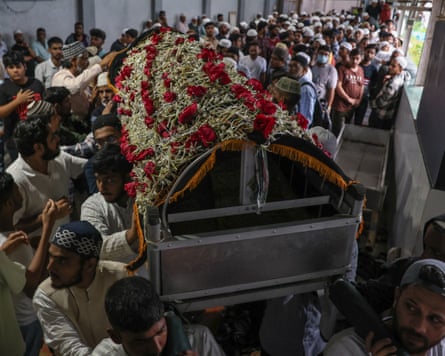A funeral in India, with a large group of mourners carrying and touching a flower-adorned coffin