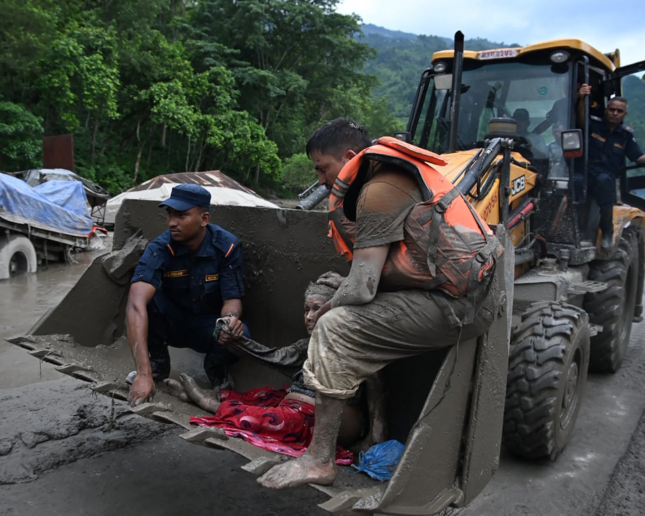 Two men accompany an elderly woman in the bucket of a digger