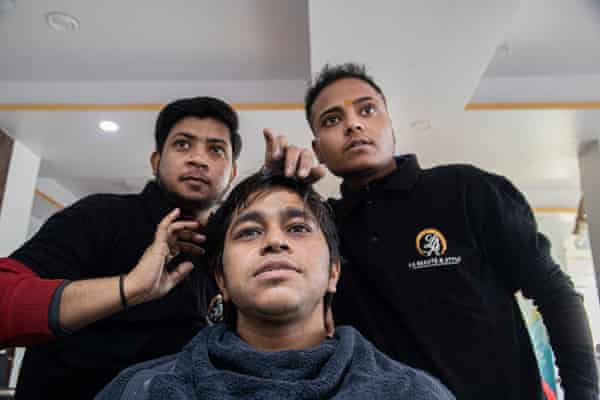 A man looks in a mirror while two hair stylists stand behind him