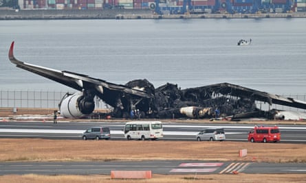 Officials look at the burnt wreckage of a Japan Airlines (JAL) passenger plane on the tarmac at Tokyo International Airport at Haneda