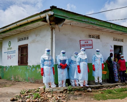 People in PPE from head to foot outside low white building