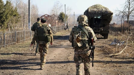 Russian soldiers on patrol on dirt road with military vehicle in foreground