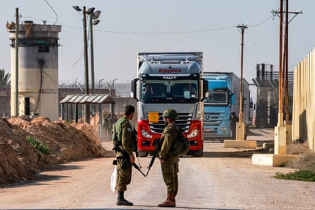 Israeli soldiers stand guard as trucks carrying humanitarian aid move at the Israeli side of the Kerem Shalom border crossing.