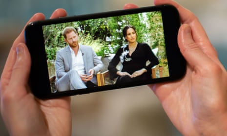 A man watches the Duke and Duchess of Sussex interview with Oprah Winfrey on a phone screen. 
