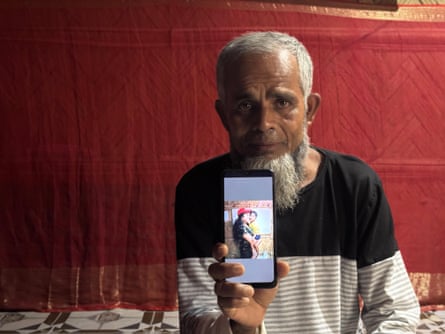 A sad-looking old man with a phone showing a photo of a woman and child