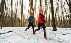 Posed by models Man and Woman Running Together Through Woods in Winter. Smiling Couple Running Along Trail Through Forest on Cold Winter Day.