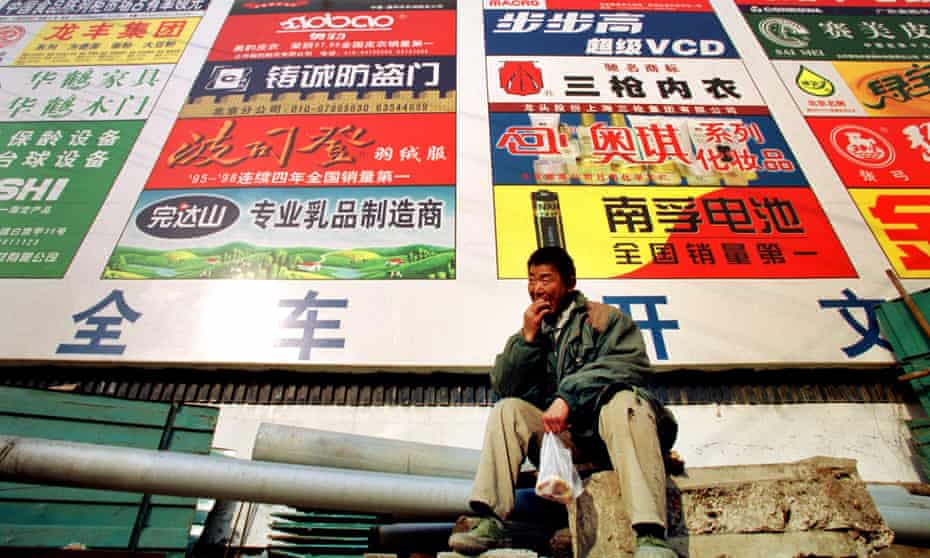 A worker rests in front of a billboard which promotes Chinese brands in Beijing.