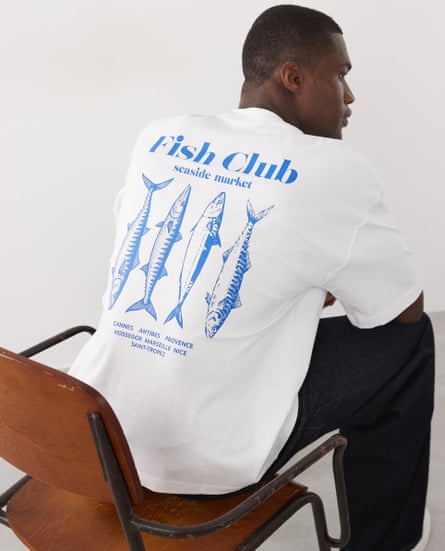 Male model sits on a chair with his back to the camera showing off a print on back of T-shirt that has four fishes under the words ‘fish club’