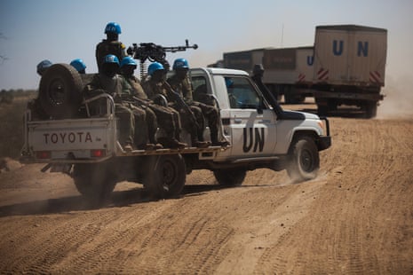 A UN pickup truck mounted with a heavy machine gun carrying a unit of blue-helmeted peacekeepers follows UN trucks in a desert landscape