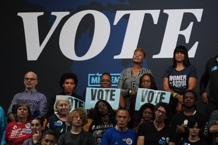 People hold signs that say Vote, in front of wall sign that says Vote.