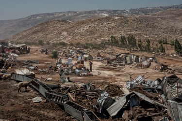 A man stands amid the remains of destroyed shelters