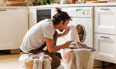 Young black man sits on floor near washing machine while doing laundry in kitchen