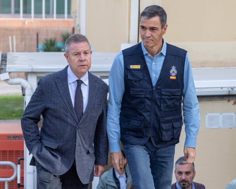 Pedro Sánchez and Emiliano García-Page walk together outdoors near a rescue coordination centre