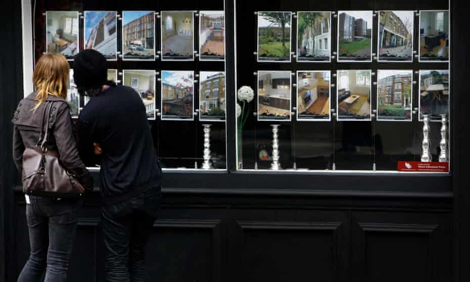 Young people look at details of properties in an Estate agents window
