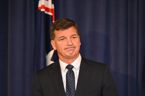 A man with dark hair stands in front of blue curtains